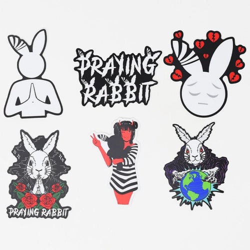 bundle of 6 praying rabbit stickers. one is the main black and white praying rabbit logo, the second is the black and white praying rabbit text logo, the third design is the sad rabbit with broken hearts above its head, the fourth design is the white rabbit praying with praying rabbit text below it, the 5th design is a red demon anime girl with a striped dress holding a gray rabbit, the 6th design is an evil white rabbit mind controlling the earth