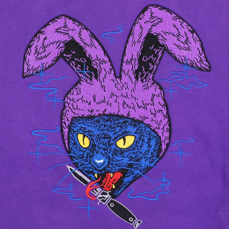 embroidered design of blue cat with purple bunny ears holding a knife in its tongue