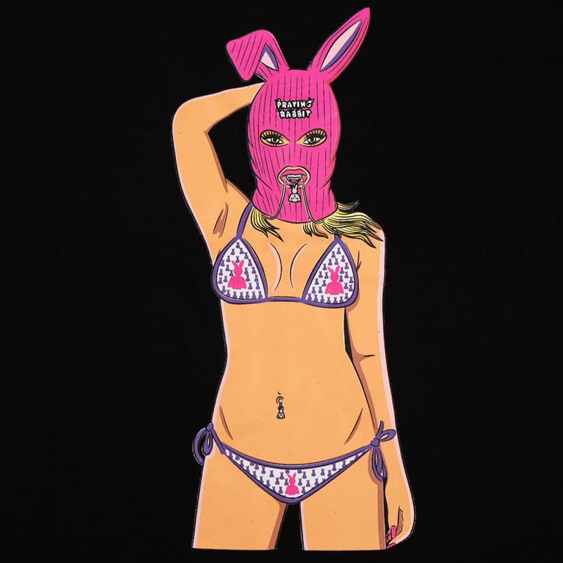 close up view of lola. she has a pink ski mask on her head, a purple and pink praying rabbit bikini. and she is biting a praying rabbit necklace.