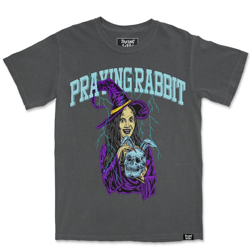 Short sleeve printed shirt with a witch graphic in which she is holding a rabbit skull. There is light blue text above the design that reads Praying Rabbit. The shirt is a vintage faded grey wash color.