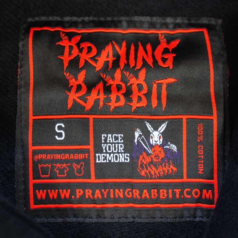 woven label that reads praying rabbit and face your demons. it shows the white rabbit stabbing the demon