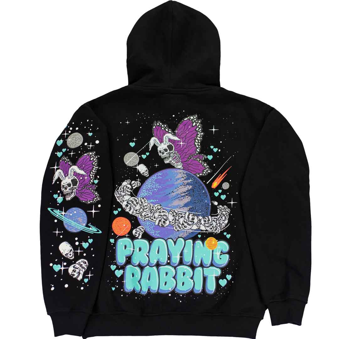 back view of black graphic hoodie that shows a skeleton rabbit butterfly flying over the planet saturn. there are a numerous amount of skulls flying around the planet like rings. throughout the design are hearts, comets, sparkles, and skulls. below the graphic is blue bubble text that reads praying rabbit. the left sleeve has a printed graphic of the same rabbit skull butterfly with purple wings, planets, spakrles, hearts, and skulls