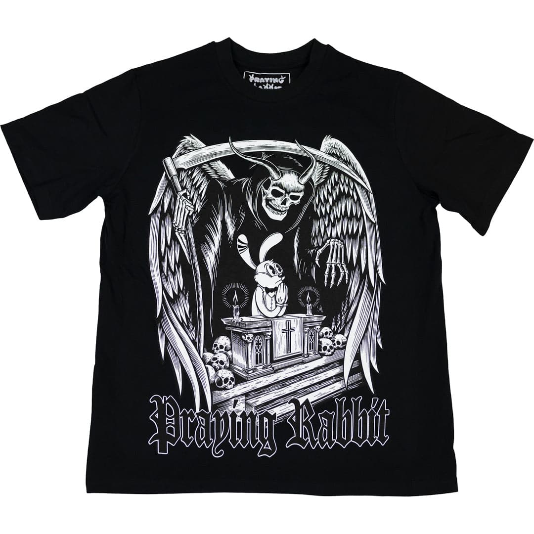 front view of black graphic t shirt of a cartoon praying rabbit on an altar. behind the praying rabbit is a huge guardian angel skeleton watching over the praying rabbit. the guardian angel is holding a scythe