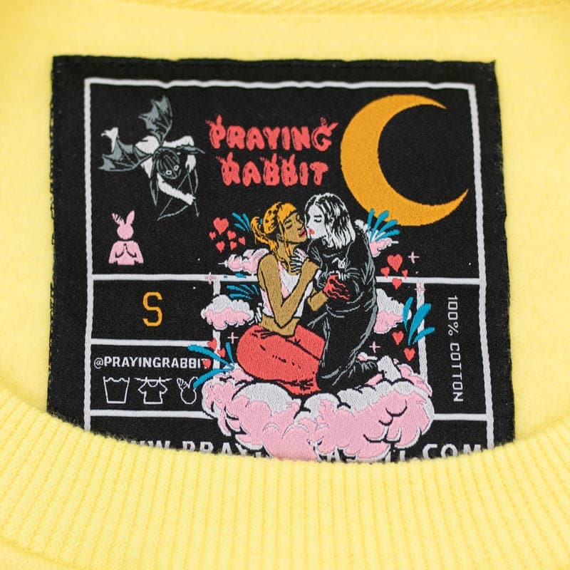 woven label that reads praying rabbit and sows the moon, two girls hugging each other on a cloud, and a cupid rabbit angel
